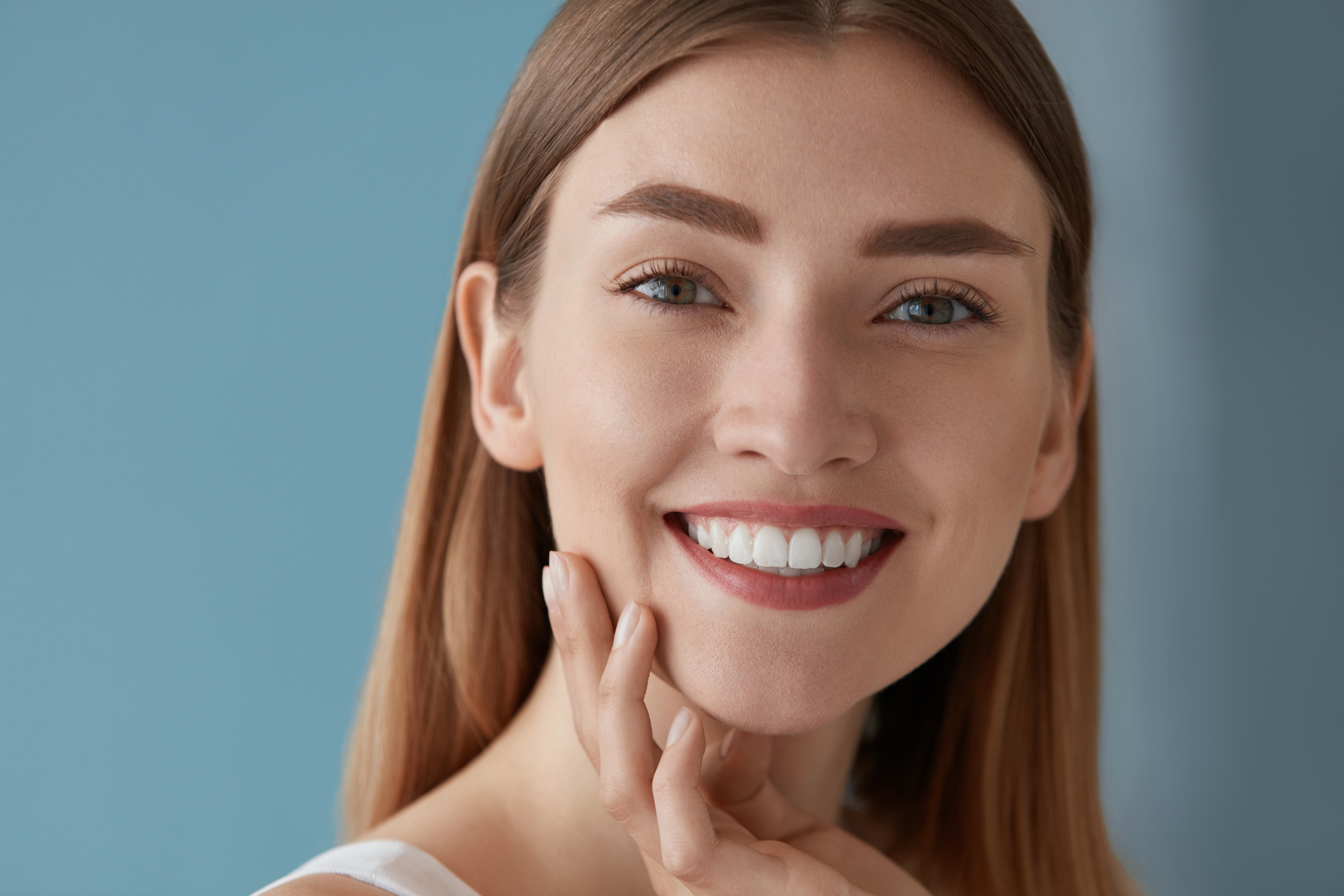 Smiling woman with straight teeth and clear aligners, showcasing a confident smile against a soft blue background, representing the benefits of orthodontic treatment at Bond Orthodontics.